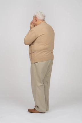Side view of an old man in casual clothes covering mouth with hands