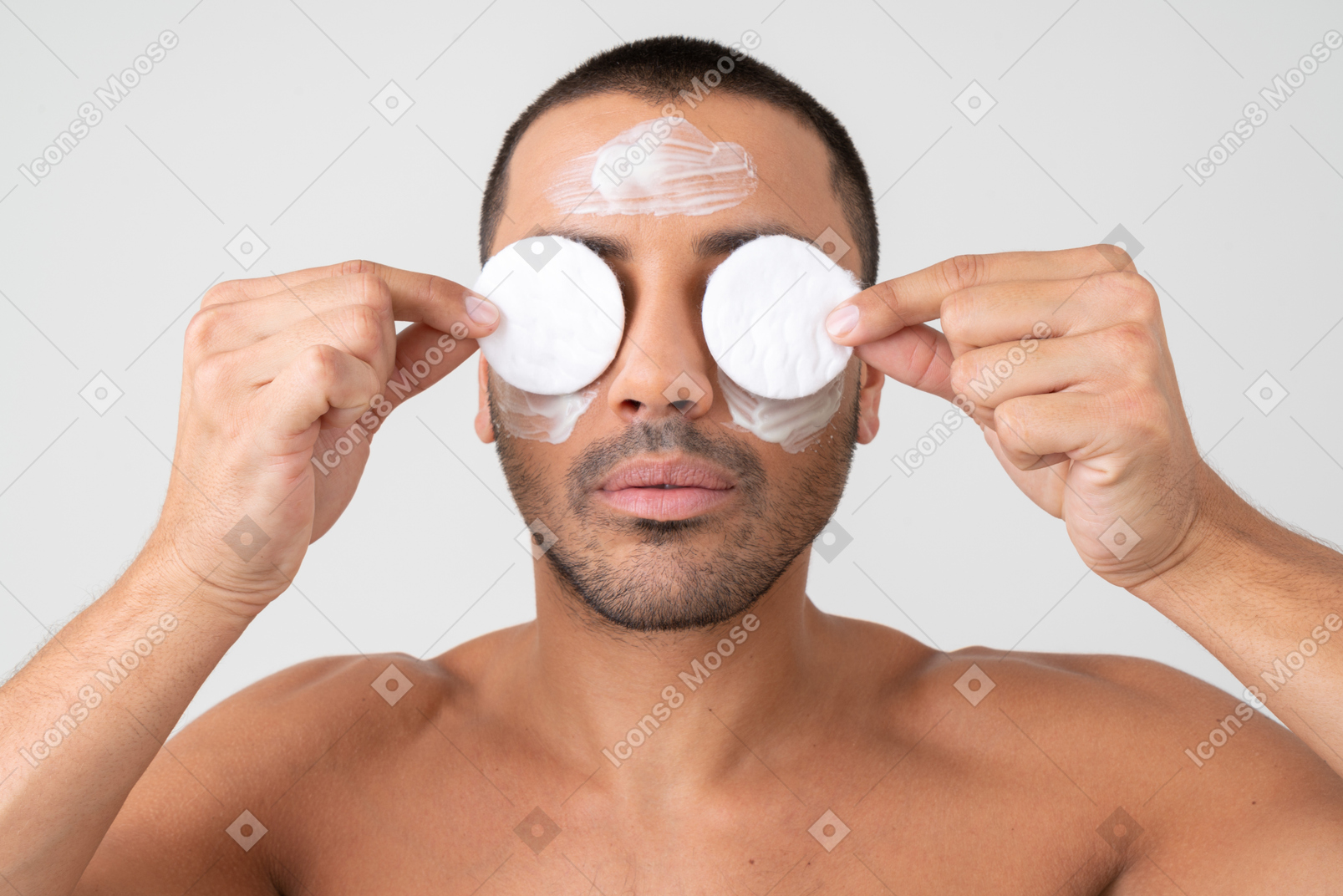 Attractive young man holding cotton pads on his eyes