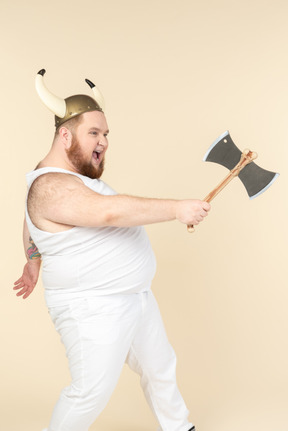 An emotional plus-sized man in white with a horned helmet on his head, holding a double-bladed axe