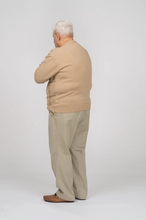 Side view of an old man in casual clothes standing with crossed arms