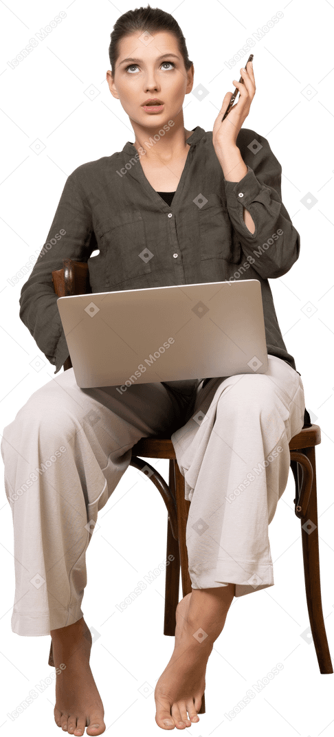 Vue de face d'une jeune femme choquée assise sur une chaise avec un ordinateur portable et un mobile