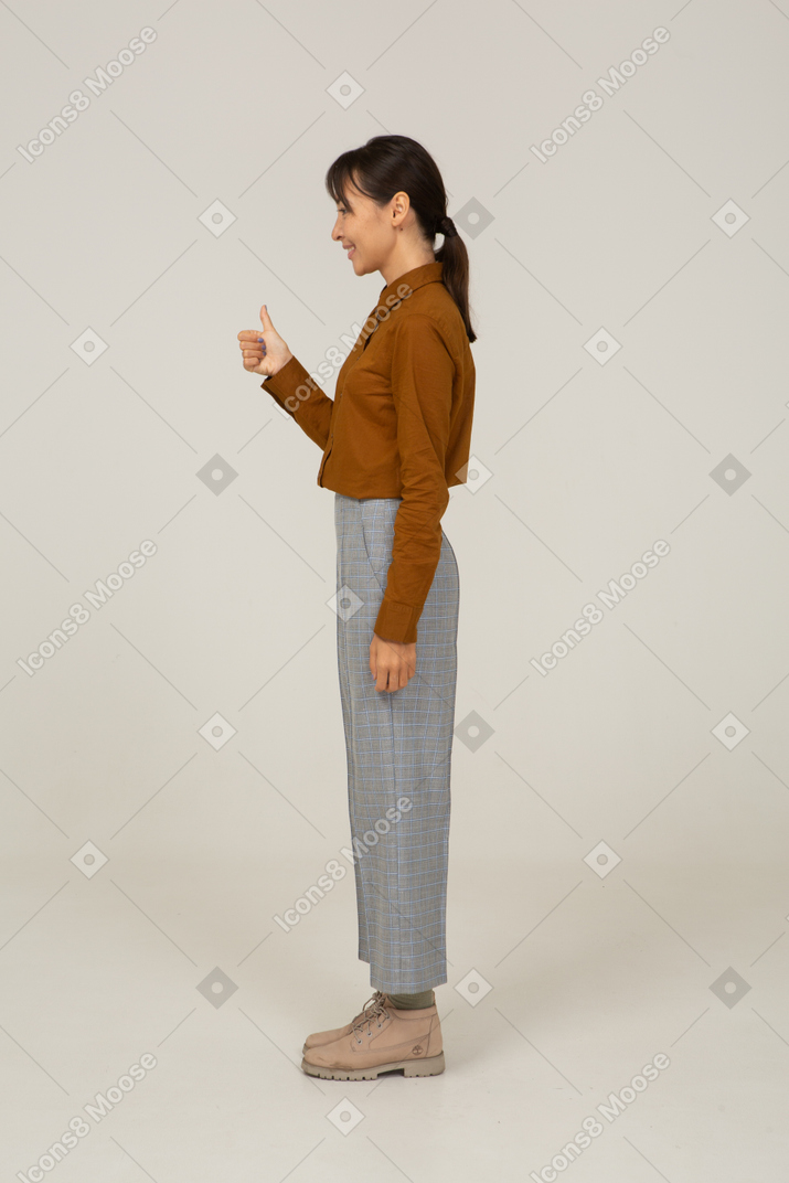 Vista lateral de una joven mujer asiática en calzones y blusa mostrando el pulgar hacia arriba