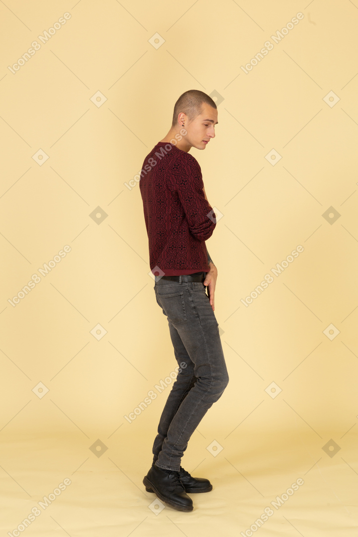 Vista laterale di un giovane uomo triste in pullover rosso che osserva da parte