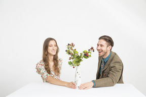 Pareja sentada en la mesa y comiendo moras de las ramas en el florero