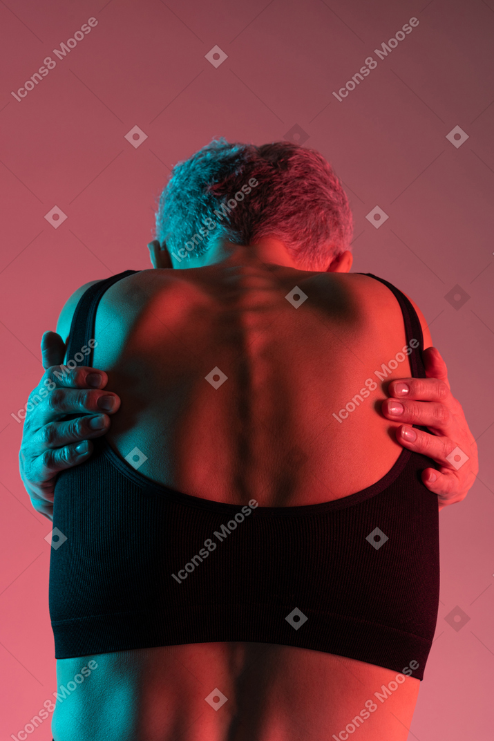 Unrecognizable short haired mature lady embracing herself back to camera