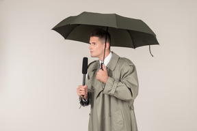 Smiling male reporter holding microphone and standing under the umbrella