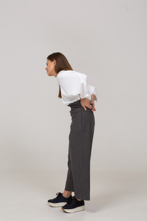 Vista laterale di una giovane donna in abiti da ufficio con mal di schiena