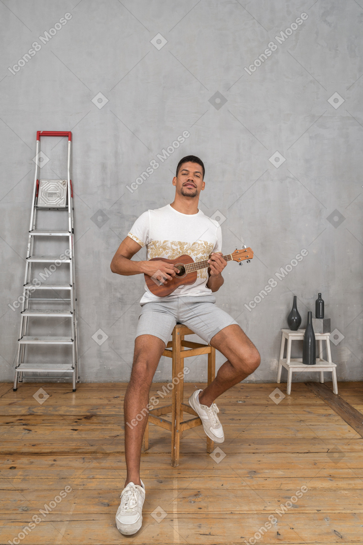 Front view of a man sitting on a stool playing ukulele