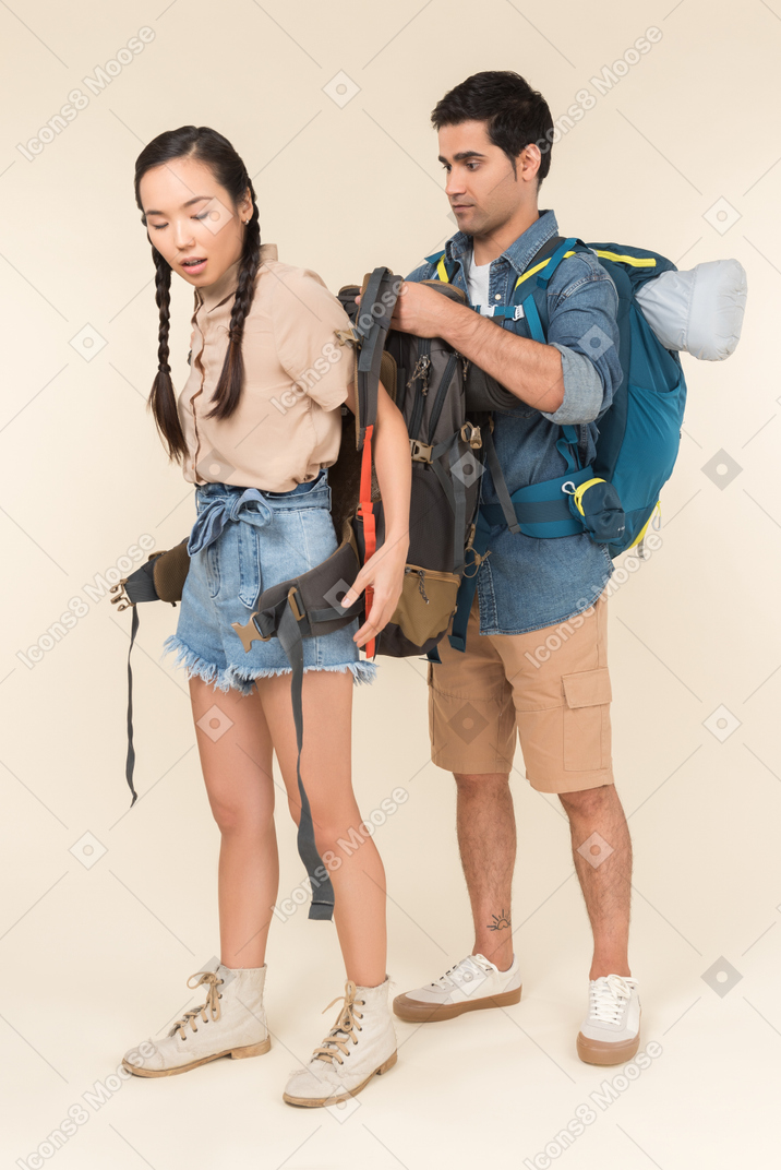 Young man helps taking off backpack to his asian girlfriend