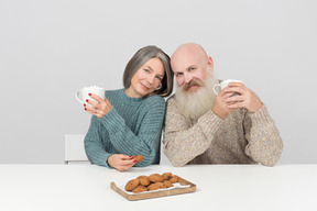Пожилая пара держит чашки и сидит из стороны в сторону