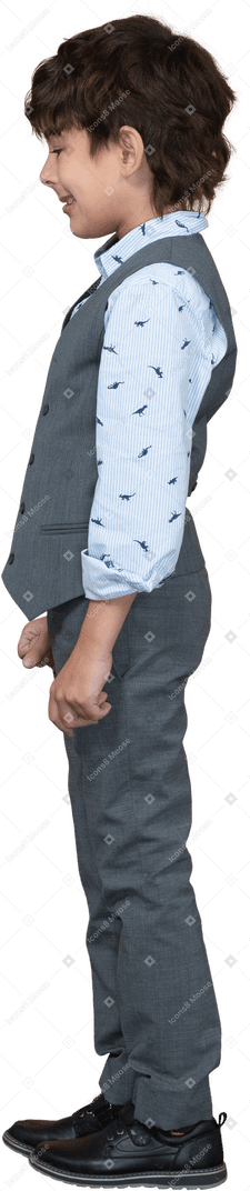 Вид сбоку на симпатичного мальчика в сером костюме, стоящего со сжатыми кулаками