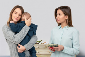 A woman holding a baby while another woman standing next to her