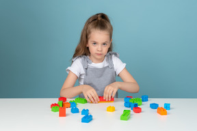 Маленькая девочка играет со строительными блоками и смотрит в камеру