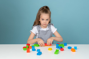 Menina brincando com blocos de construção e olhando para a câmera