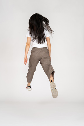 바지와 그녀의 다리를 펼치는 티셔츠에 점프하는 젊은 아가씨의 3/4보기