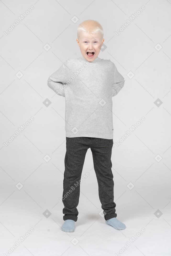 Front view of a happy kid boy screaming while putting hands on hips