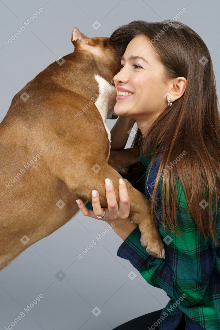 Side view of a smiling female in checked shirt hugging her bulldog