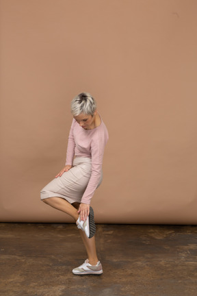 Vista lateral de una mujer en ropa casual de pie sobre una pierna y tocando su zapato