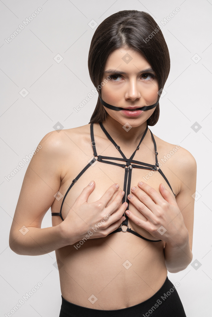 Front view of sexy young woman in harness covering breast with