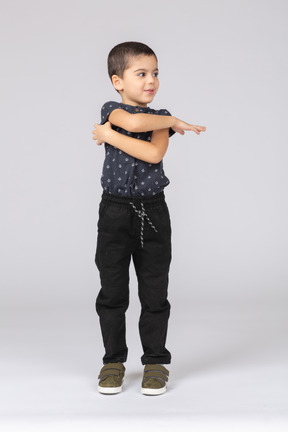 Vista frontal de um lindo menino em pé com os braços cruzados e olhando para o lado