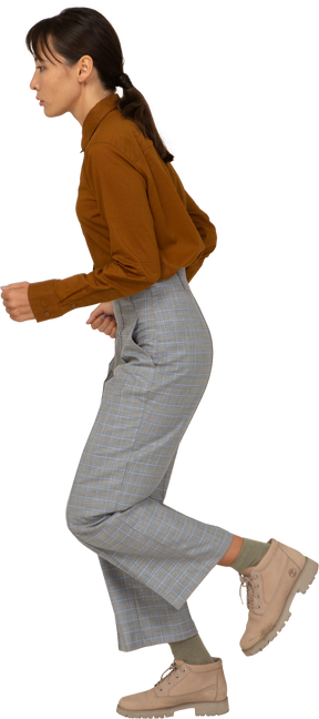 Vista laterale di una giovane donna asiatica in corsa in calzoni e camicetta