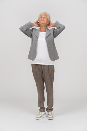 Front view of an old lady in suit posing with hands behind head