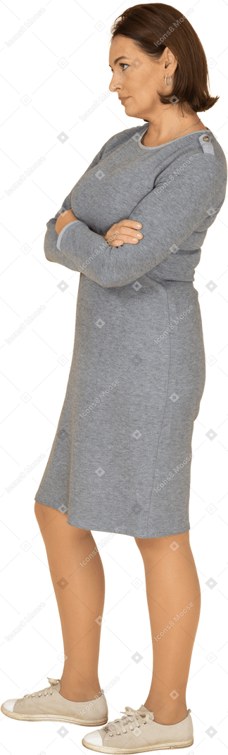 Vue latérale d'une femme en robe grise debout avec les bras croisés