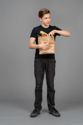 Young man looking sideways while getting a vegetable out of a paper bag