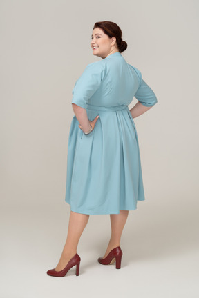 Vue latérale d'une femme heureuse en robe bleue debout avec les mains sur les hanches