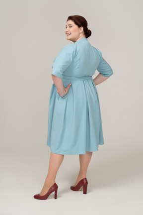 Side view of a happy woman in blue dress standing with hands on hips