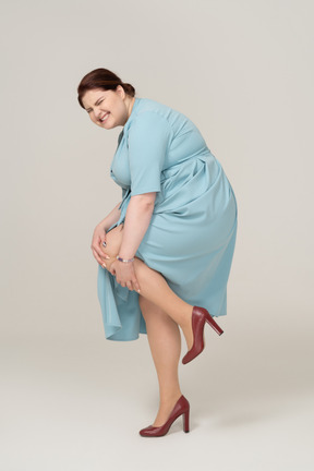 Vista lateral de uma mulher de vestido azul tocando seu joelho machucado