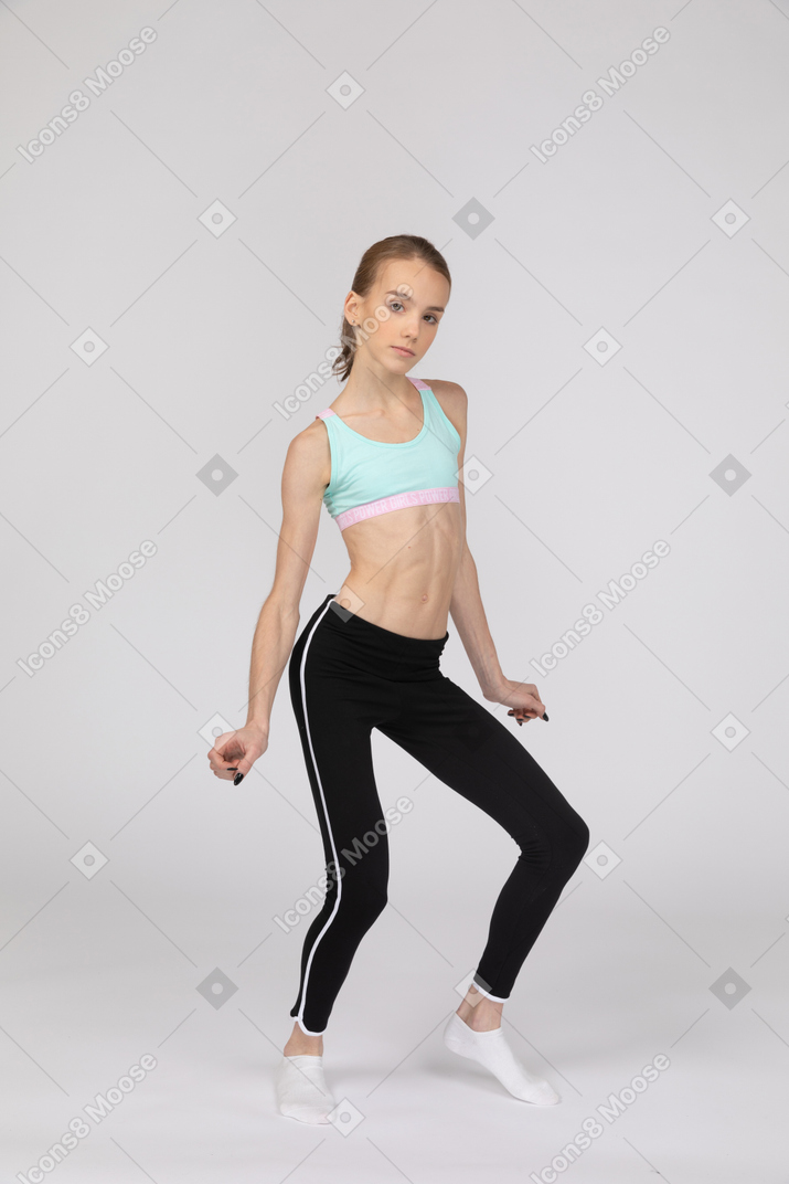 Vista de três quartos de uma adolescente em roupas esportivas, olhando para a câmera e dobrando os joelhos