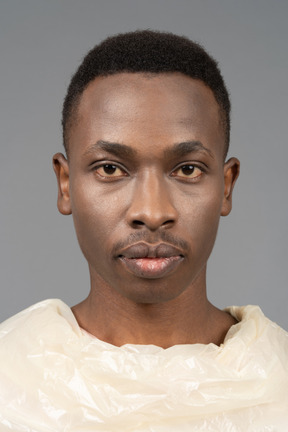 Nahaufnahmeporträt eines ernsten afrikanischen mannes, der in plastik eingewickelt wird