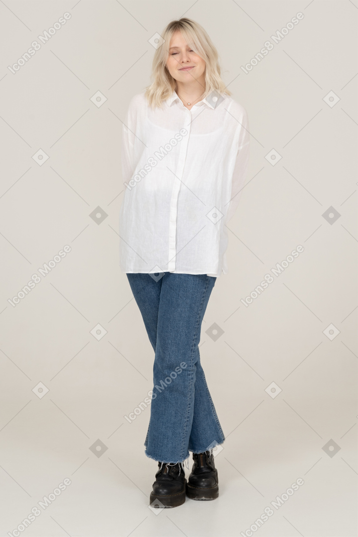 Vista frontal de una mujer rubia tímida en ropa casual cruzando las piernas con los ojos cerrados