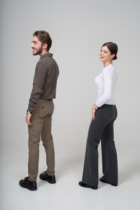 Vista posterior de tres cuartos de una pareja joven sonriente en ropa de oficina