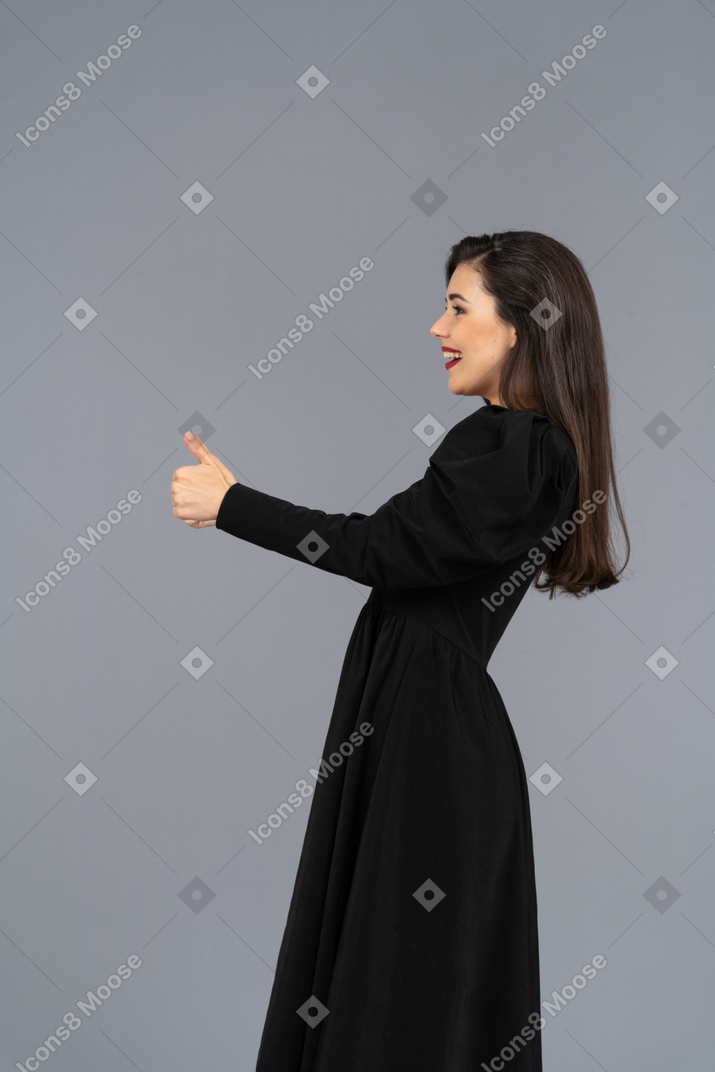 Vista laterale di una giovane donna sorridente in un abito nero che mostra un pollice in su