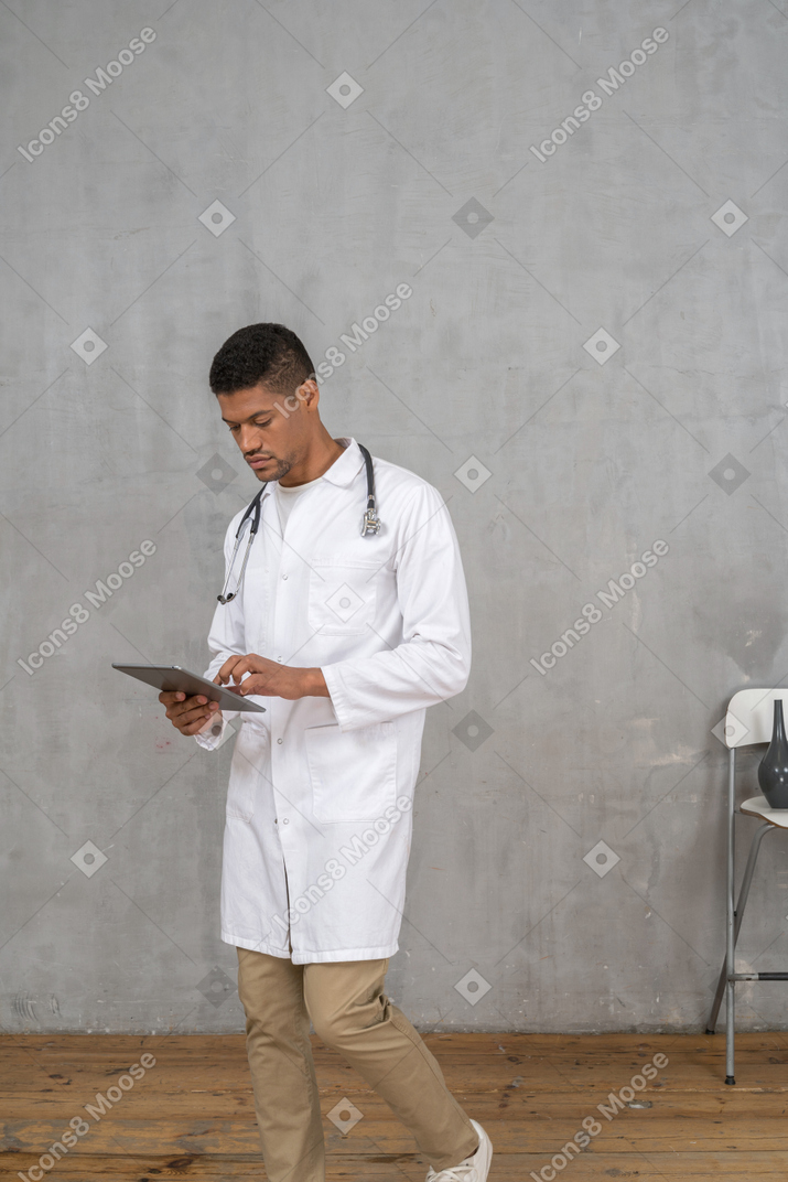 Médico varón mirando la tableta mientras camina