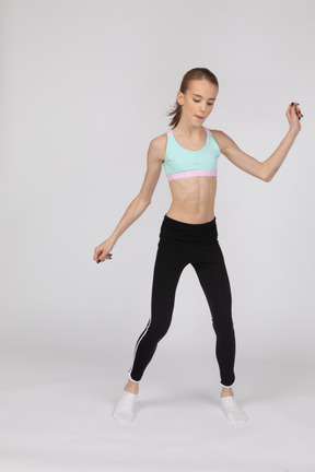 Vista frontal de uma adolescente em roupas esportivas pulando enquanto dança