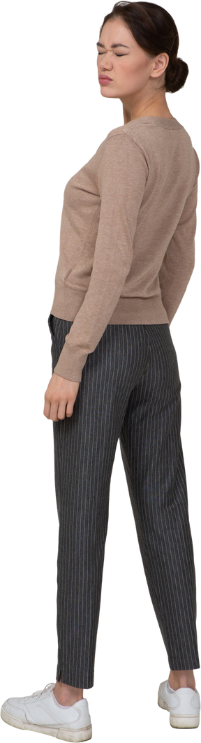 Vista posterior de tres cuartos de una joven en suéter y pantalones de pie con los ojos cerrados