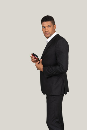 Vista laterale di un giovane in abito nero che tiene in mano una carta di credito