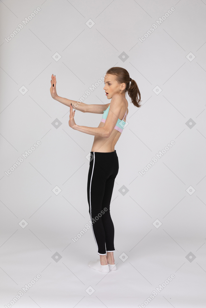 Vista posterior de tres cuartos de una jovencita en ropa deportiva extendiendo las manos