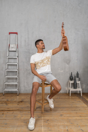 Front view of a man on a stool holding up a ukulele