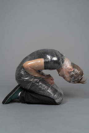 Young man on his knees wrapped in plastic