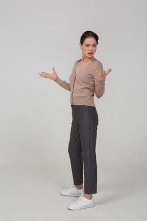 Вид в три четверти вопрошающей жестикулирующей молодой леди в бежевом пуловере