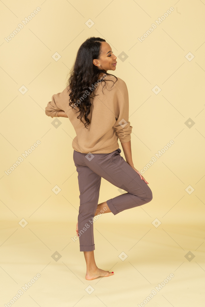 Three-quarter back view of a  grimacing young dark-skinned female putting hand on hip