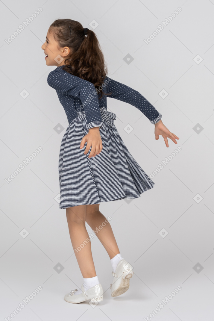 Una mujer con un vestido azul de pie delante de una pared con las piernas cruzadas