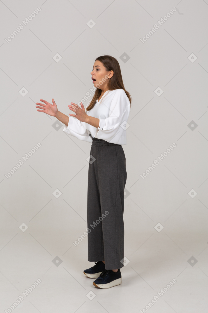 Three-quarter view of a shocked young lady in office clothing raising hands