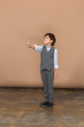 Front view of a cute boy in grey suit standing with outstretched arm