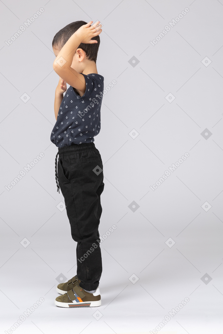 Вид сбоку мальчика, стоящего с рукой на голове