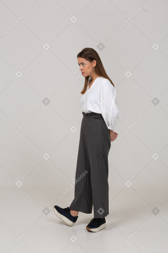 Three-quarter view of a displeased young lady in office clothing holding hands behind